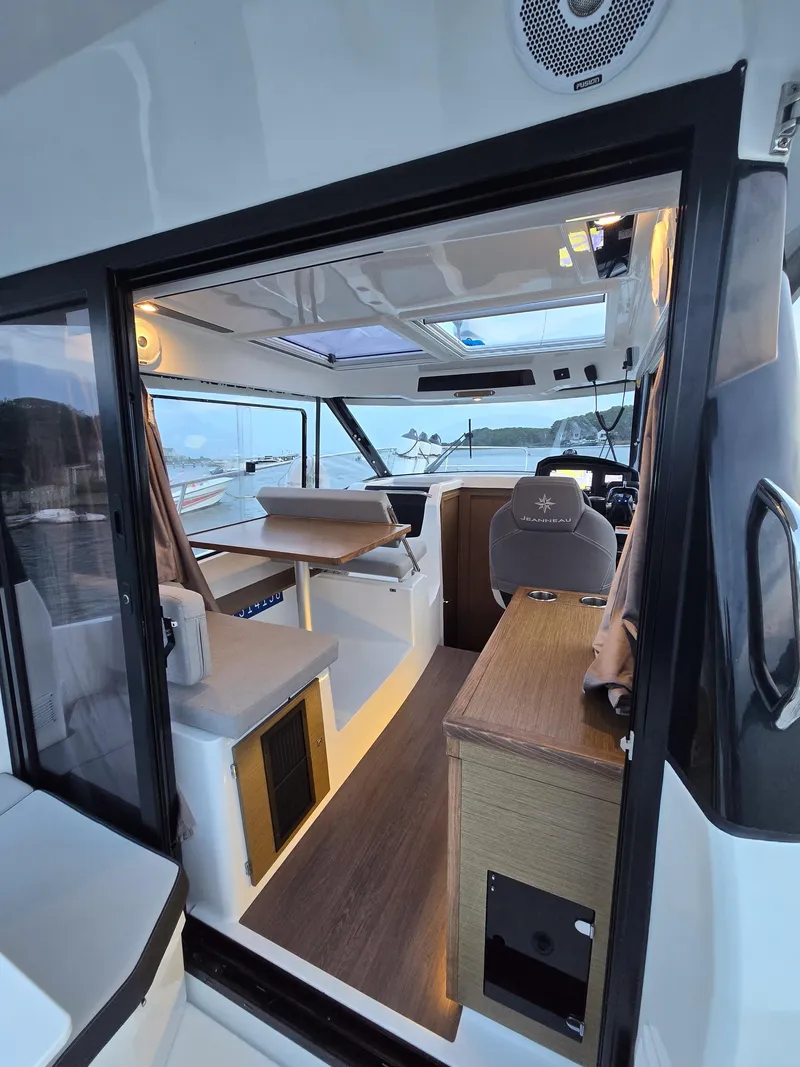 Slide: The Image of 2021 Jeanneau NC895 interior with modern seating and navigation area, overlooking a serene waterfront. - 28