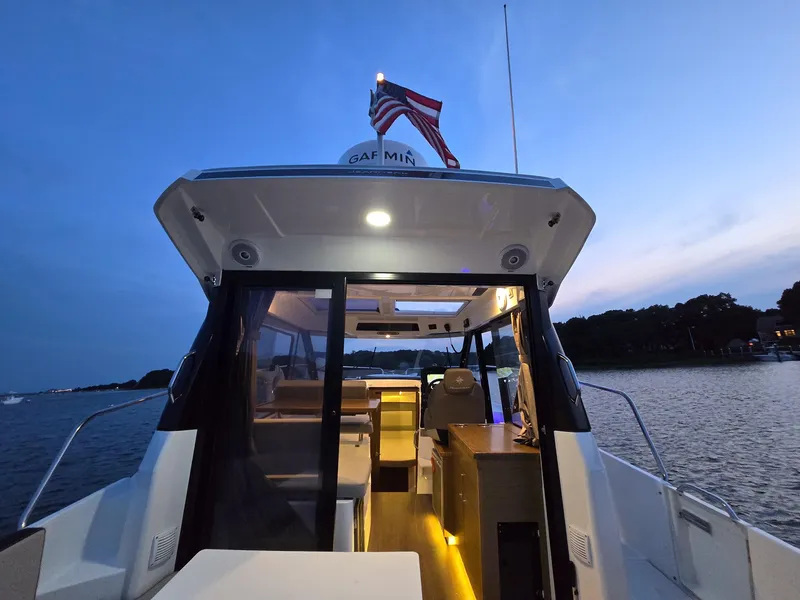 Slide: The Image of 2021 Jeanneau NC895 boat at sunset, featuring illuminated interior and American flag. - 3