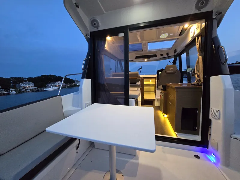 Slide: The Image of 2021 Jeanneau NC895 boat interior with seating and table, illuminated at dusk. - 4