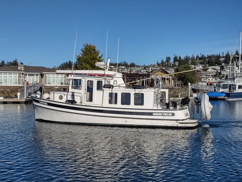 Slide: The Image of 2006 Nordic Tug 32 boat docked in a scenic marina setting. - 2