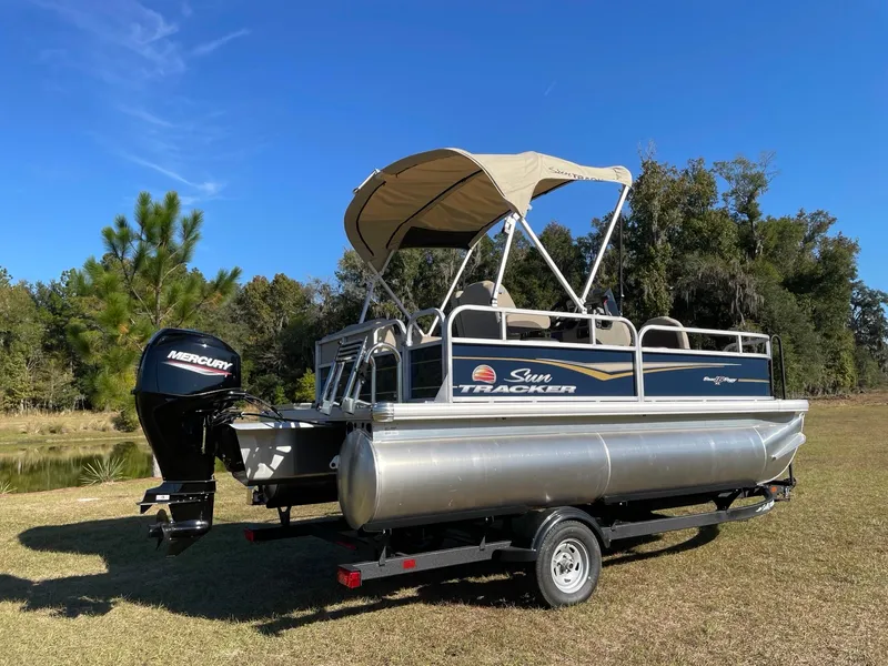 Slide: The Image of 2025 Sun Tracker Bass Buggy 16 XL Select pontoon boat on grassy field. - 2