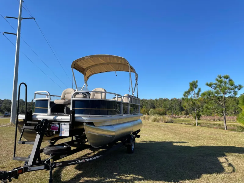 Slide: The Image of 2025 Sun Tracker Bass Buggy 16 XL Select pontoon boat on trailer, parked on grass. - 3