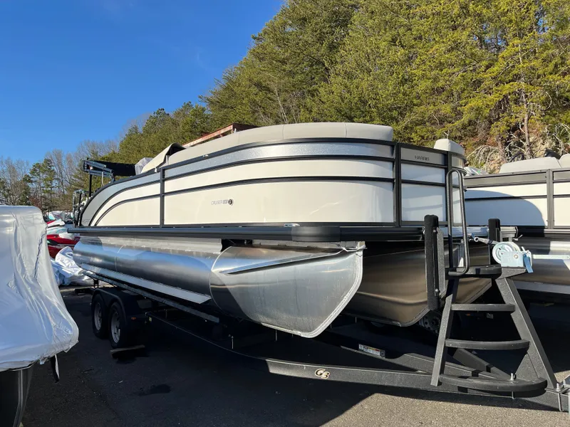 The Image of 2025 Harris Cruiser 230 pontoon boat on trailer, surrounded by trees and clear blue sky. - 0