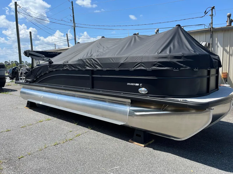 Slide: The Image of 2025 Harris Cruiser 230 pontoon boat with black cover, parked outdoors. - 4