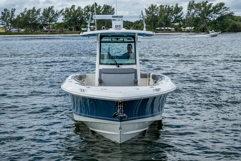 Slide: The Image of 2023 Boston Whaler 330 Outrage boat on water, front view, with trees in background. - 7