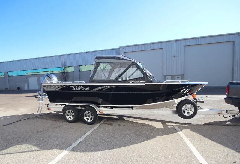 Slide: The Image of 2025 Weldcraft 210 Revolution Soft Top boat on trailer, parked outdoors. - 2