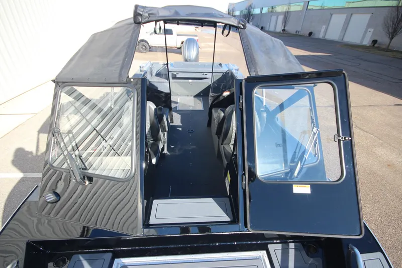 Slide: The Image of 2025 Weldcraft 210 Revolution Soft Top boat with open cabin doors, parked outdoors. - 33