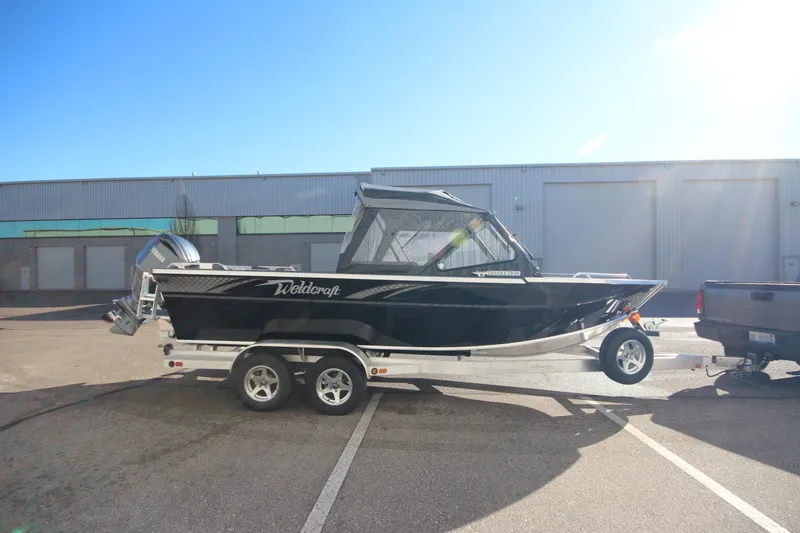 Slide: The Image of 2025 Weldcraft 210 Revolution Soft Top boat on trailer, parked outdoors. - 4