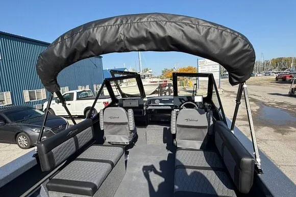 Slide: The Image of 2025 Weldcraft 210 Revolution boat interior with seating and canopy, docked outdoors. - 13