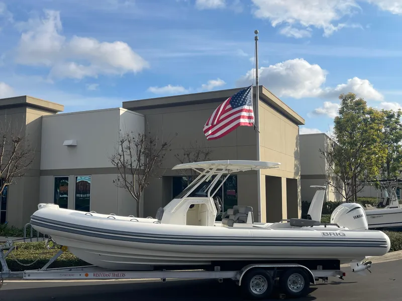 The Image of 2025 Brig Eagle 8 boat on trailer, American flag, modern building background. - 0