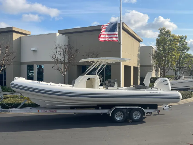 Slide: The Image of 2025 Brig Eagle 8 boat on trailer, parked outside building with American flag. - 2