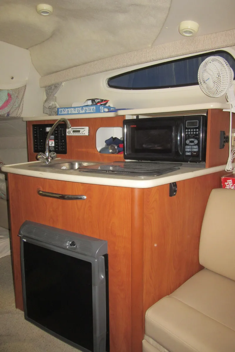 Slide: The Image of 2004 Bayliner 245 boat interior with kitchenette, featuring sink, microwave, and mini-fridge. - 14