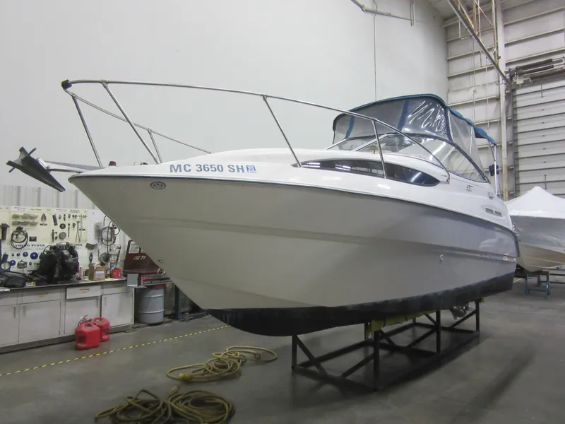 Slide: The Image of 2004 Bayliner 245 boat in a warehouse, elevated on a stand for maintenance. - 2