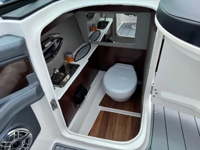 Slide: The Image of 2021 Chaparral 267 SSX OB boat interior with compact bathroom, sink, and wooden flooring. - 14