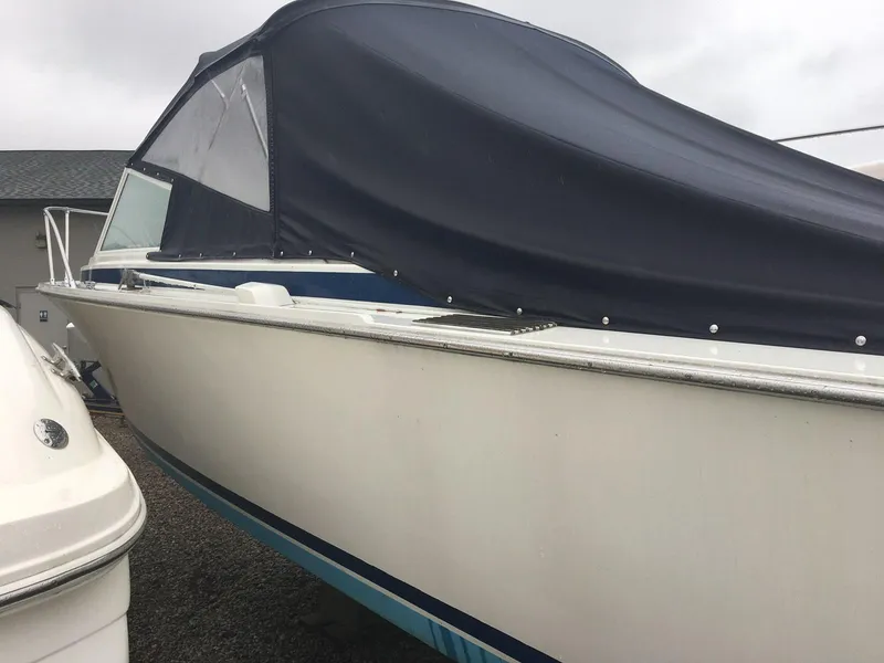 Slide: The Image of 1976 Bertram 26 Moppie boat with a dark cover, parked outdoors. - 5