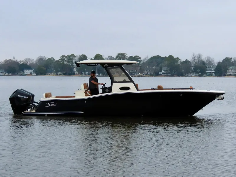 Slide: The Image of 2023 Scout 277 LXF boat cruising on a calm lake with a person at the helm. - 5