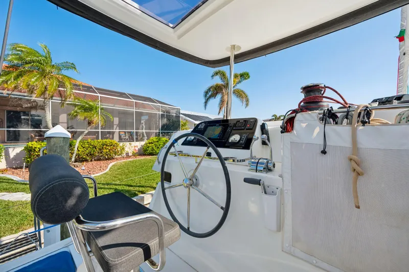 Slide: The Image of Cockpit of 2019 Lagoon 42 catamaran with steering wheel and control panel, docked near palm trees. - 14
