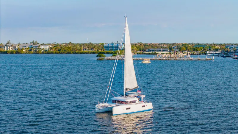 Slide: The Image of 2019 Lagoon 42 catamaran sailing on a calm blue sea near a coastal town. - 2