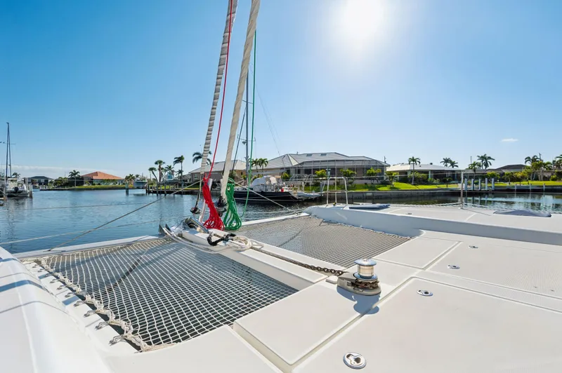 Slide: The Image of 2019 Lagoon 42 catamaran on sunny waterfront, showcasing deck and netting. - 23