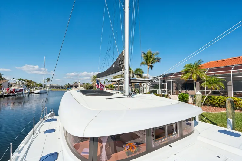 Slide: The Image of 2019 Lagoon 42 catamaran docked by a canal, surrounded by palm trees and waterfront homes. - 29