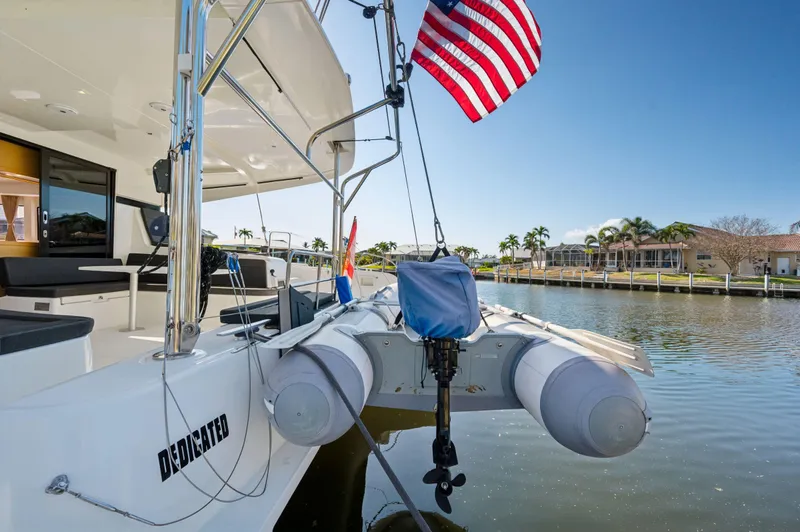 Slide: The Image of 2019 Lagoon 42 catamaran with dinghy and American flag on a sunny waterfront. - 46