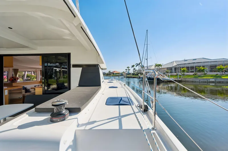 Slide: The Image of 2019 Lagoon 42 catamaran docked by a serene waterfront, showcasing spacious deck and modern design. - 48