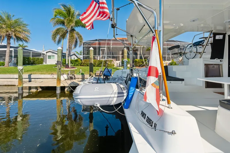 Slide: The Image of 2019 Lagoon 42 catamaran docked, featuring flags and a small dinghy. - 49