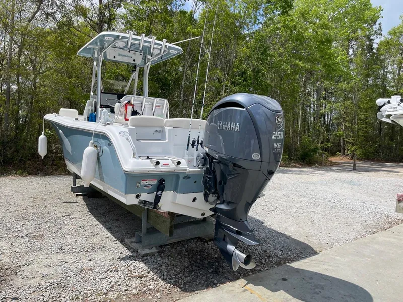 Slide: The Image of 2022 Sea Hunt 234 Ultra boat with Yamaha 250 engine, parked on gravel near trees. - 2