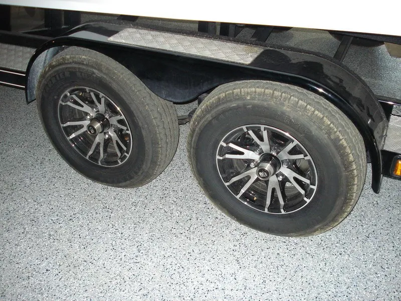 Slide: The Image of Trailer wheels of 2024 Nautique Super Air Nautique G23 on a speckled floor. - 8