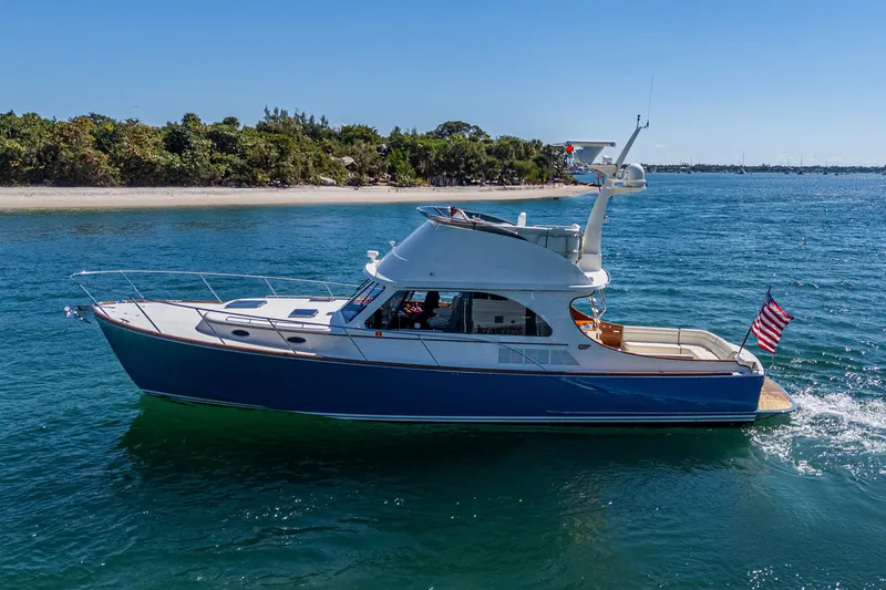 Slide: The Image of 2019 Hinckley Talaria 43 Flybridge yacht cruising on blue water near a sandy shoreline. - 3