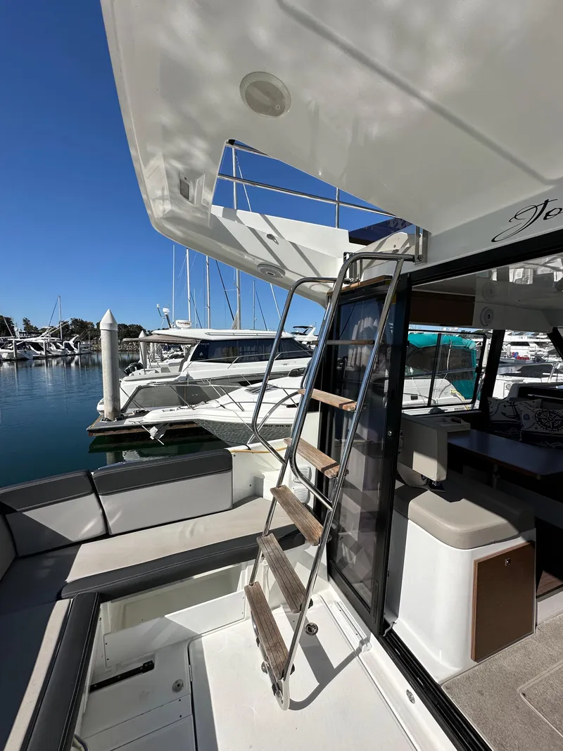 Slide: The Image of 2021 Jeanneau NC 1095 Fly yacht, exterior view with ladder and marina background. - 12