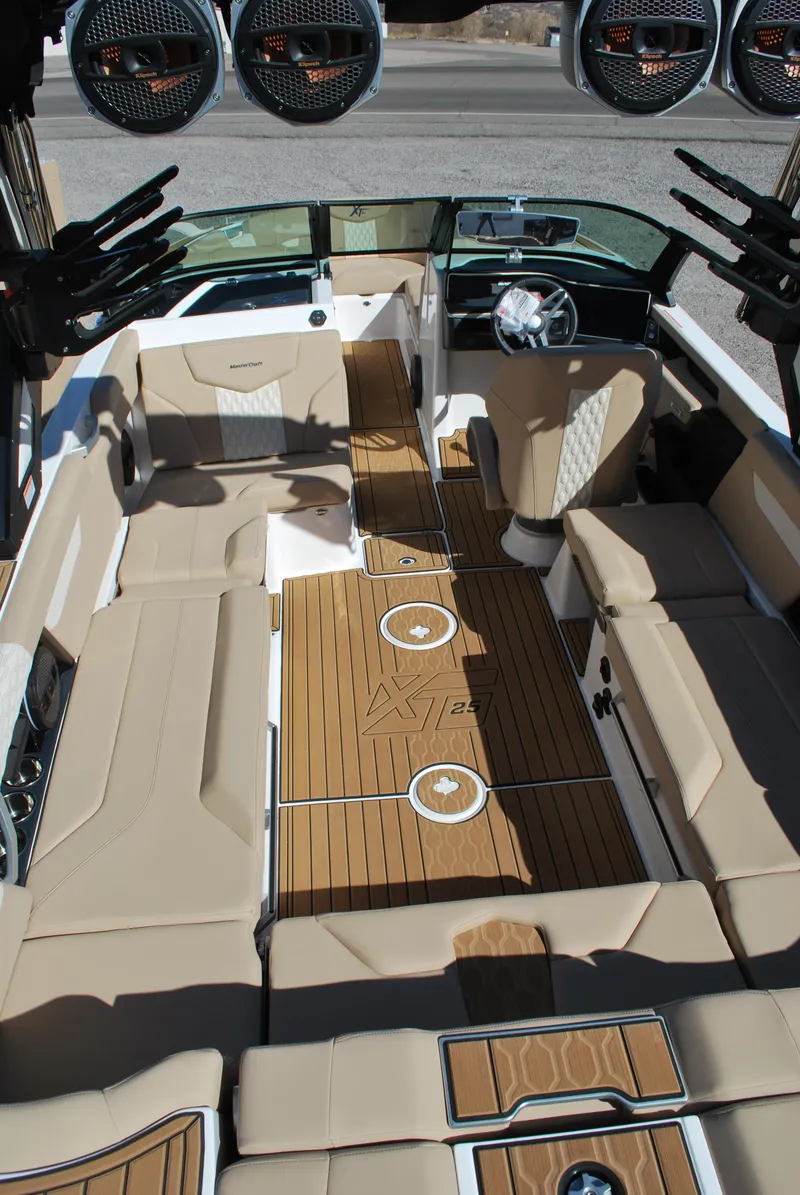 Slide: The Image of 2025 MasterCraft XT25 boat interior with beige seating and wooden flooring. - 13