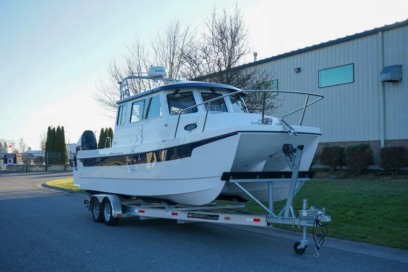 Slide: The Image of 2025 C-Dory 25' Tomcat Catamaran on trailer, parked near industrial building. - 1