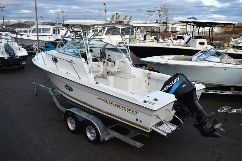 Slide: The Image of 2001 Aquasport 215 Explorer Walk-around boat on trailer, docked with other vessels. - 6