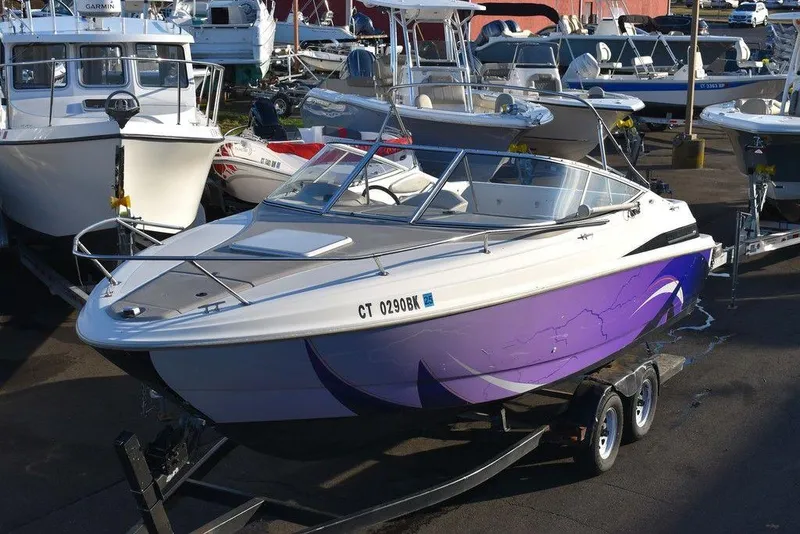 The Image of 1999 Maxum 2300SC boat with purple hull on trailer, parked among other boats. - 1