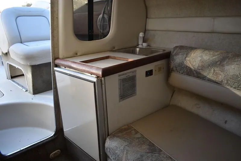 Slide: The Image of Interior of a 1999 Maxum 2300SC boat featuring a compact kitchenette and seating area. - 26