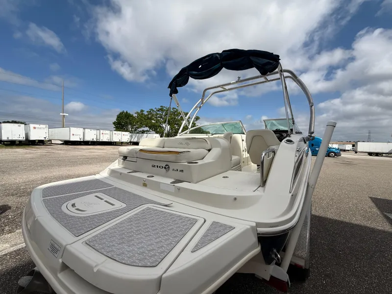 Slide: The Image of 2008 Sea Ray 210 Sundeck boat with swim platform, parked outdoors under a cloudy sky. - 24