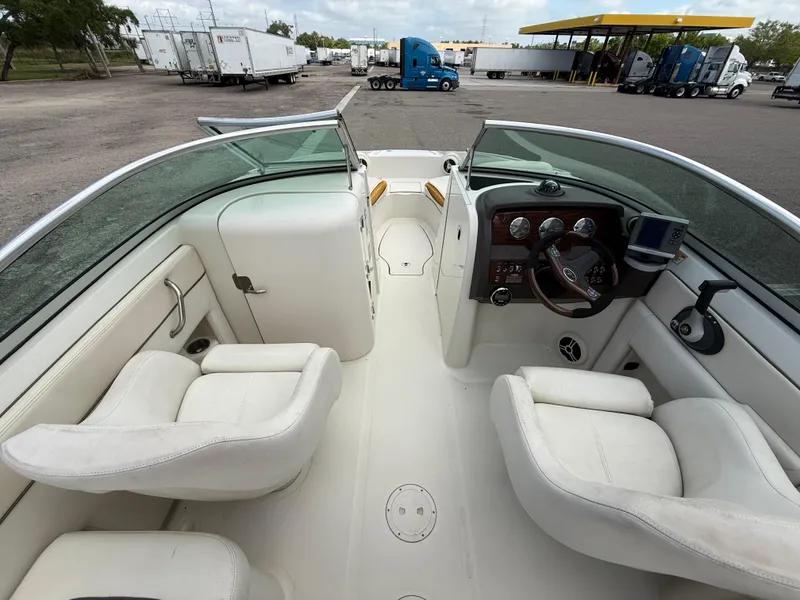 Slide: The Image of 2008 Sea Ray 210 Sundeck interior with white seating and dashboard, parked near trucks. - 38