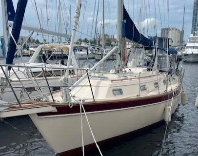 Slide: The Image of 1995 Island Packet 37 sailboat docked in marina with city skyline background. - 2