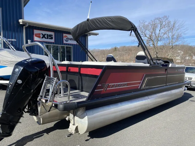 Slide: The Image of 2024 Viaggio Diamante D22U Triple pontoon boat with red and black design, parked outdoors. - 3