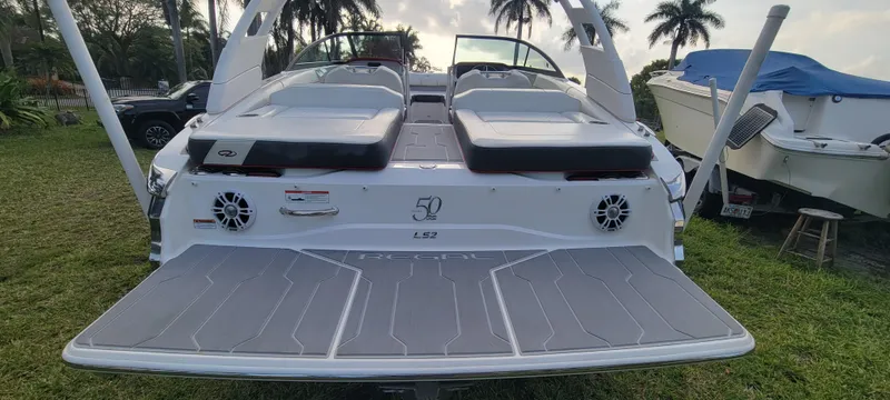 Slide: The Image of 2021 Regal LS2 boat rear view with swim platform and speakers, parked on grass. - 13