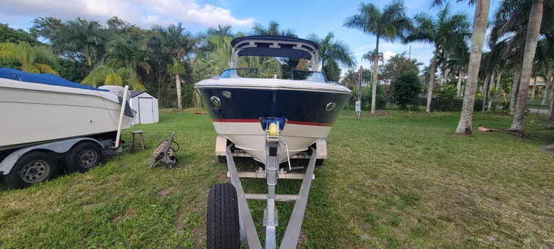 Slide: The Image of 2021 Regal LS2 boat on trailer, parked on grass with palm trees in the background. - 2