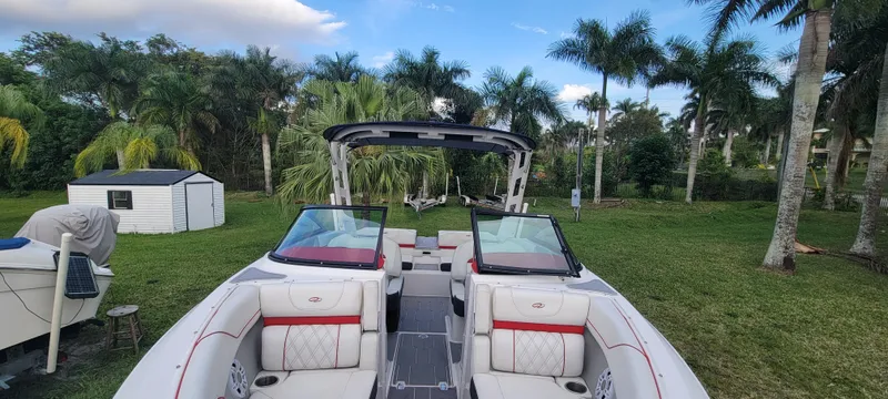 Slide: The Image of 2021 Regal LS2 boat with open seating, surrounded by lush palm trees and a small shed. - 20