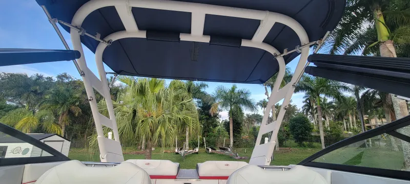 Slide: The Image of 2021 Regal LS2 boat interior with canopy, surrounded by lush palm trees. - 43