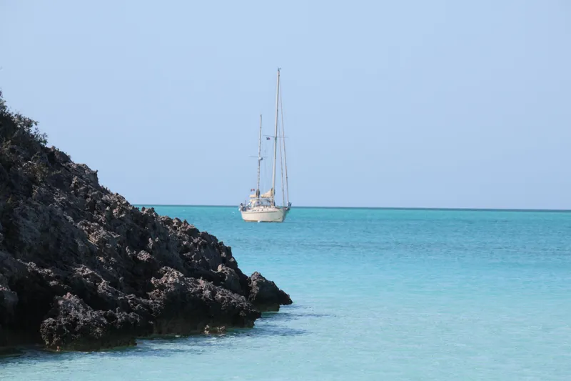 The Image of Whitby 42 Ketch sailboat on turquoise sea near rocky shore, 1983 model. - 0