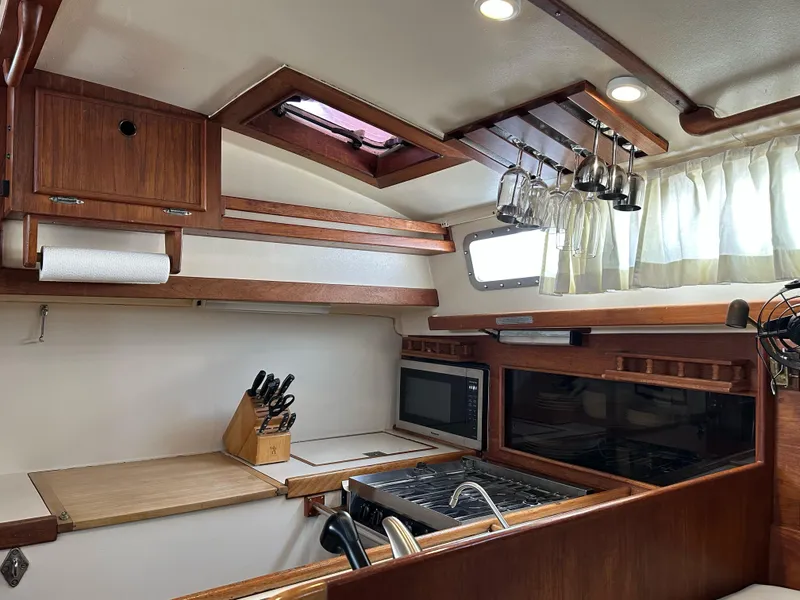 Slide: The Image of 1983 Whitby 42 Ketch kitchen with wooden cabinetry, stove, and hanging glassware. - 16