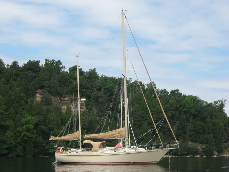 Slide: The Image of 1983 Whitby 42 Ketch sailboat on calm water, surrounded by lush greenery. - 5