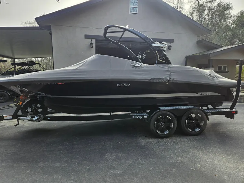 Slide: The Image of 2013 Sea Ray 230 SLX boat covered on trailer, parked in front of a house. - 23