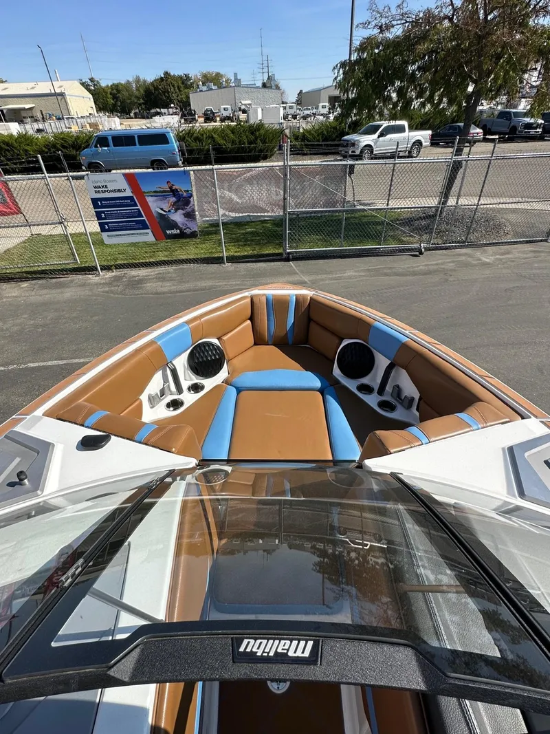 Slide: The Image of 2024 Malibu 22 LSV boat interior with brown and blue seating, parked outdoors. - 10