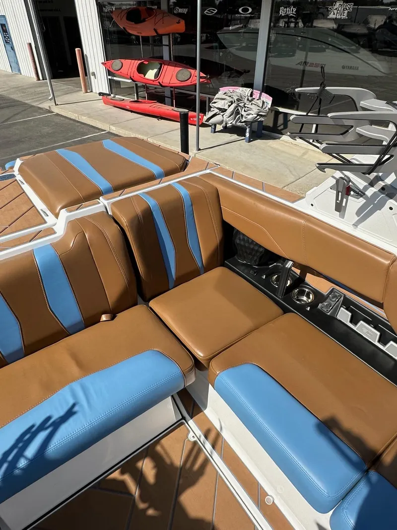 Slide: The Image of 2024 Malibu 22 LSV boat interior with brown and blue seating, docked near kayaks. - 13
